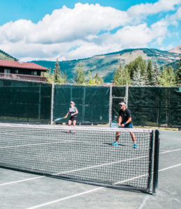 Two people playing tennis with mountain background