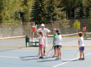 Instructor talking to children on tennis court