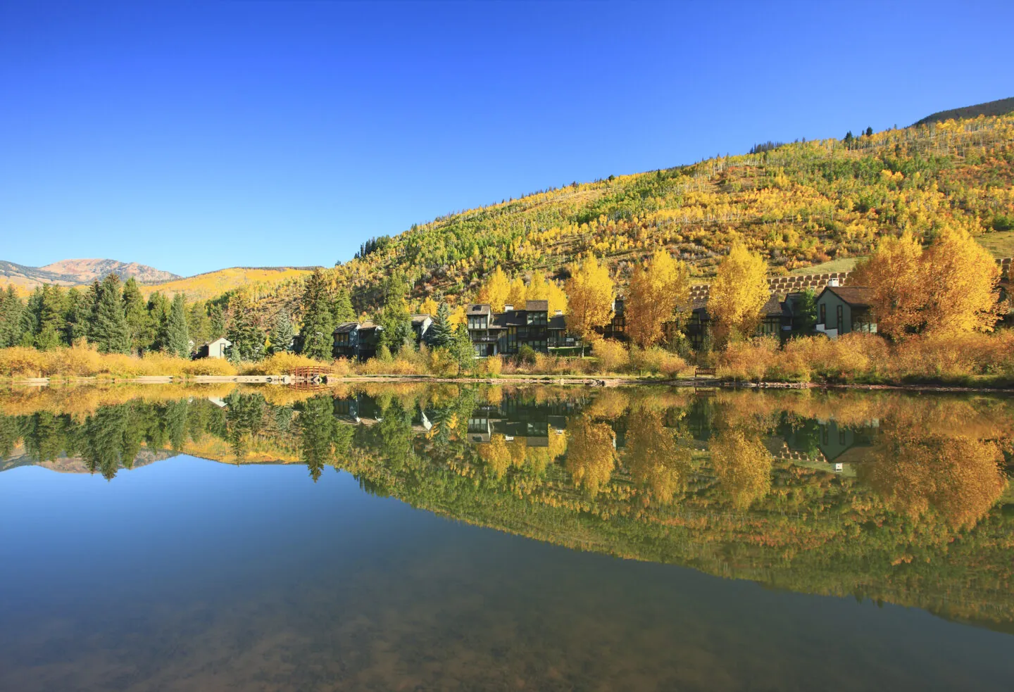 A wide exterior view of a resort with buildings and trees reflected in a lake.